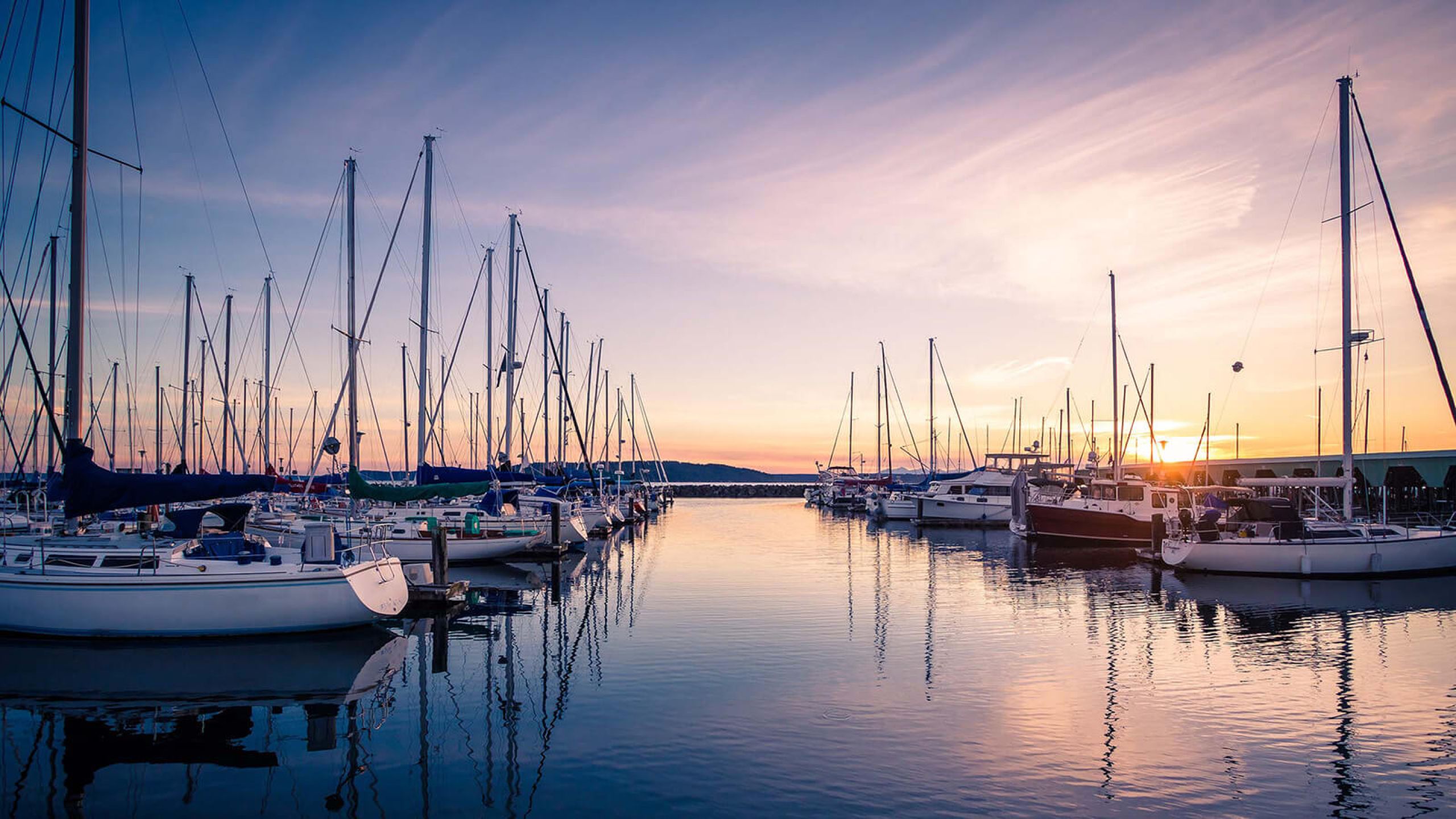 Landscape photo of marina dock with boats docked and sunrise and purplish skies and crisp ocean